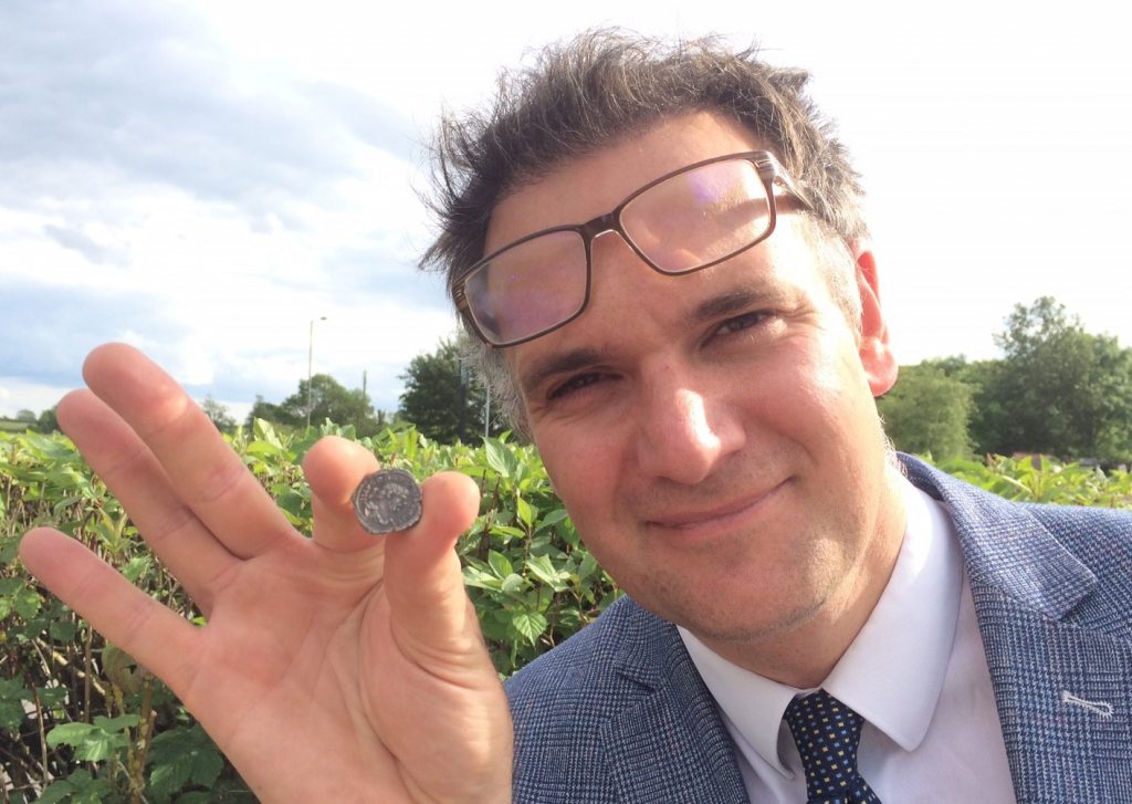 Auctioneer Charles Hanson with the tiny silver Roman coin - the only example of its kind in the world 