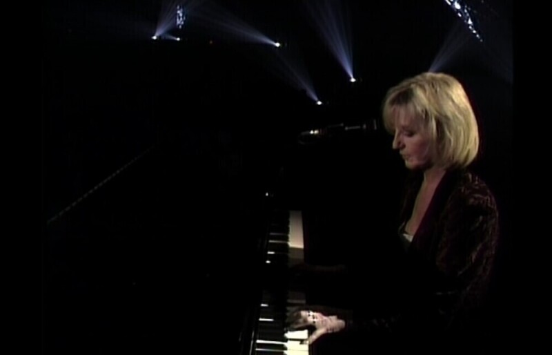 Christine McVie of Fleetwood Mac playing a piano on stage.