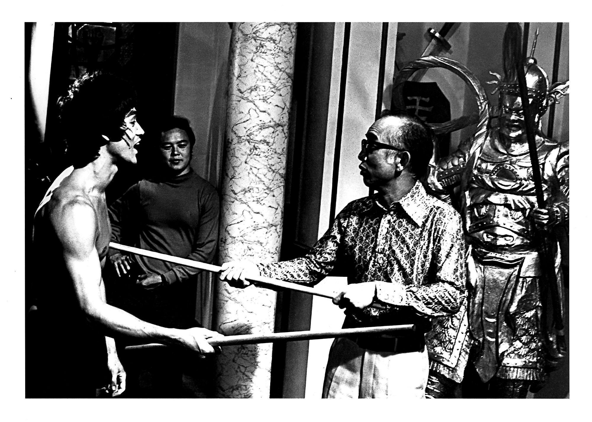 Bruce Lee filming with a bo staff.