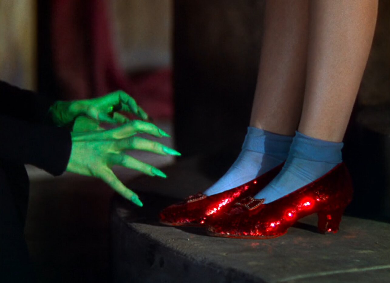 Judy Garland as Dorothy Gale wears Ruby Slippers in the Wizard of Oz. Here, the green hands of the Wicked Witch of the West can be seen grasping for them.