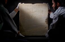 Two men carry a tablet containing an early inscription of the 10 commandments.