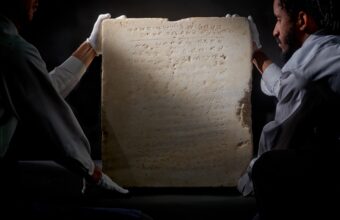 Two men carry a tablet containing an early inscription of the 10 commandments.