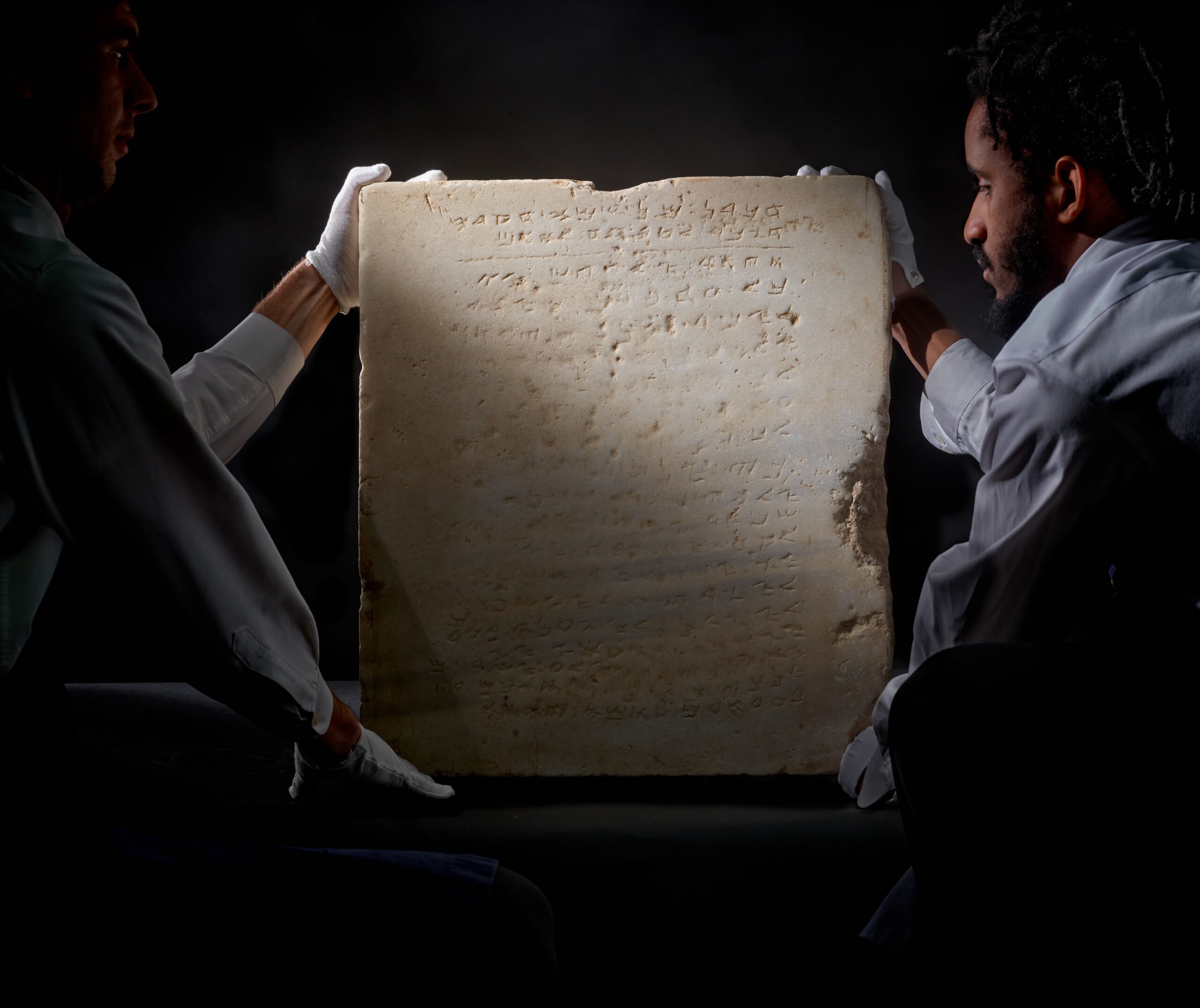 Two men carry a tablet containing an early inscription of the 10 commandments.