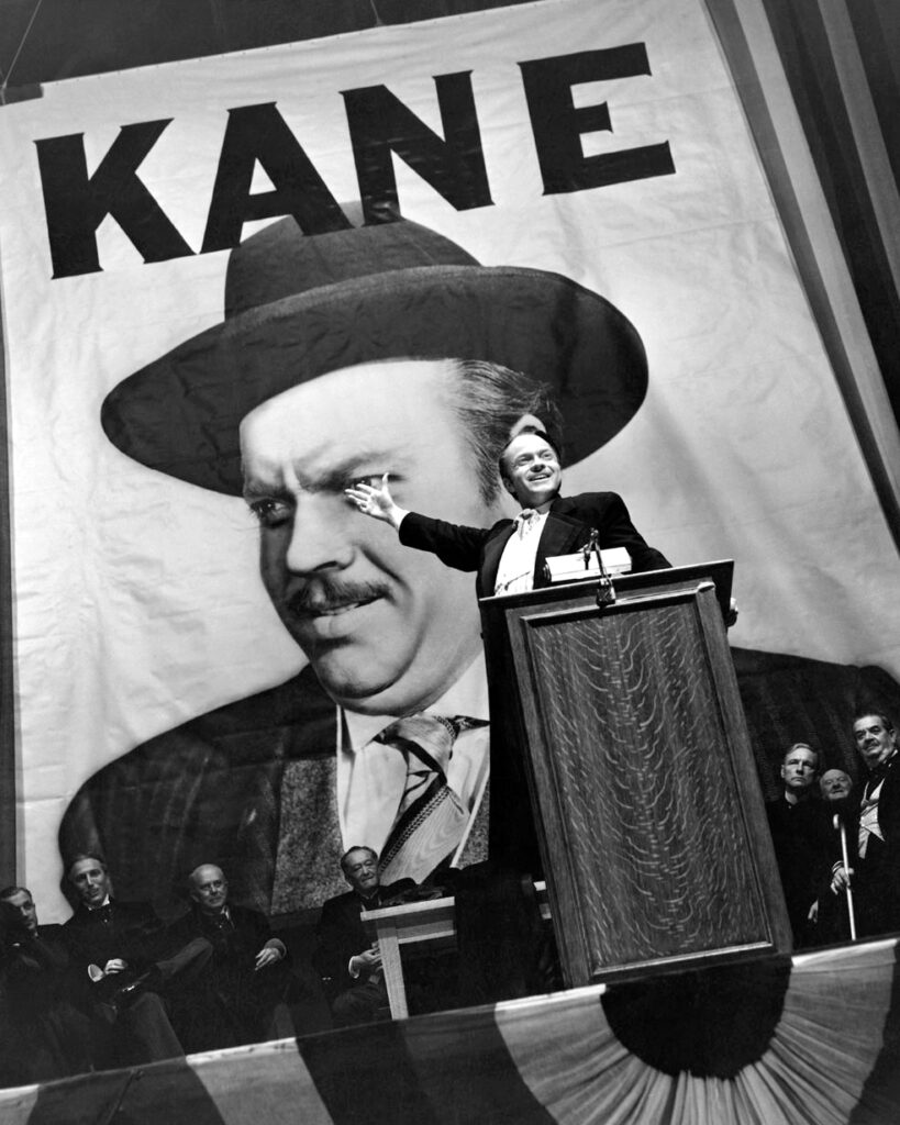 Orson Welles as Charles Foster Kane campaigning for office in front of a giant poster of himself in the movie Citizen Kane.