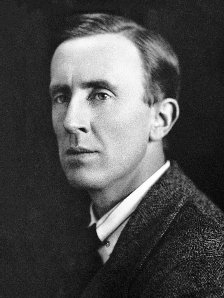 1920s black and white formal photographic portrait of author JRR Tolkien, shows him in tweed suit with white shirt and dark tie. 