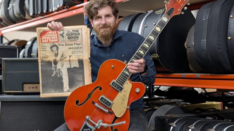 Auctioneer Luke Hobb of Gardiner Houlgate is shown holding a red semi-acoustic guitar owned by Jimmy Page of Led Zeppelin.