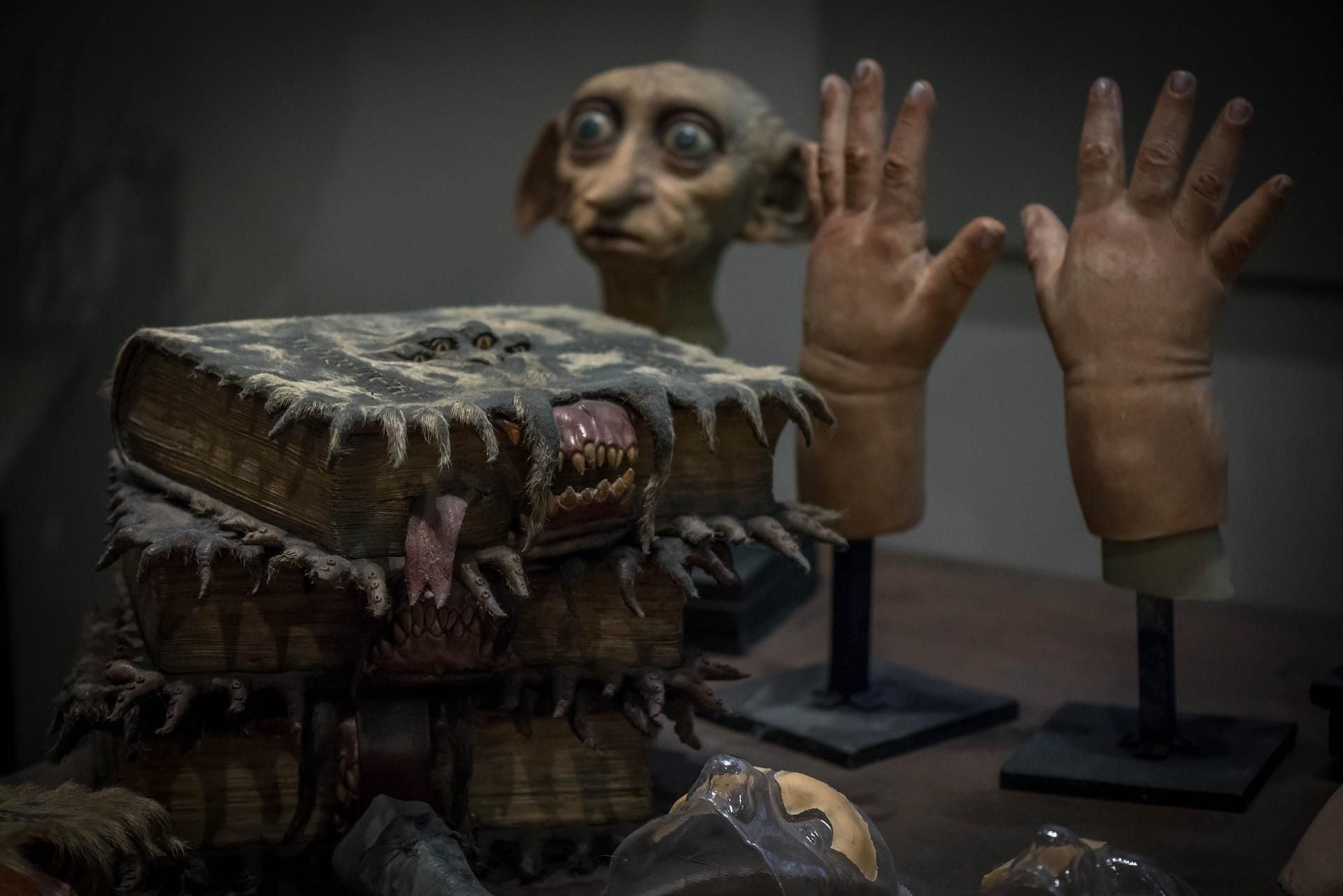 Film props featuring monster book replicas, a Dobby-style house-elf model, and a pair of prosthetic hands mounted on stands.