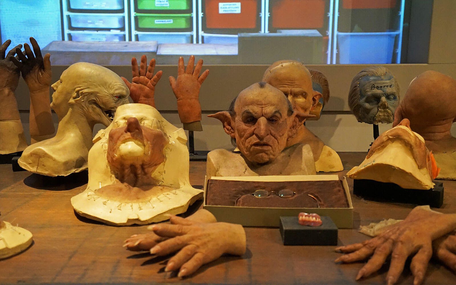 A collection of prosthetic head silicone moulds, goblin masks, and artificial hands on display in a film studio workshop.