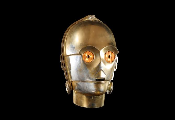 An illuminated C-3PO head piece prop set against a black background.
